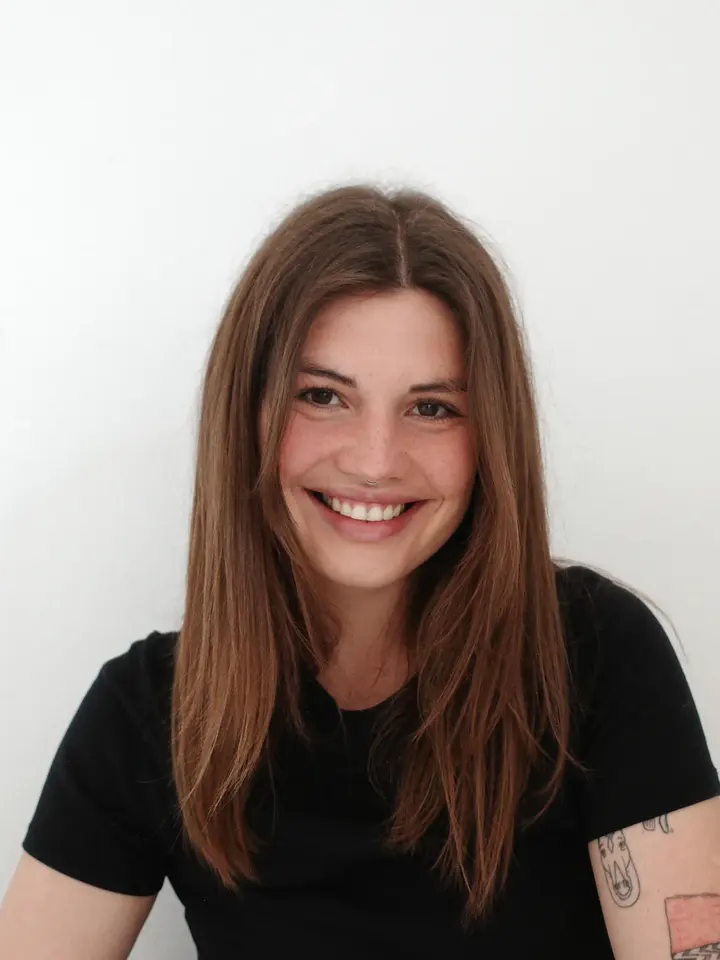 Portrait of Olga, smiling, in a black T-shirt against a pale wall