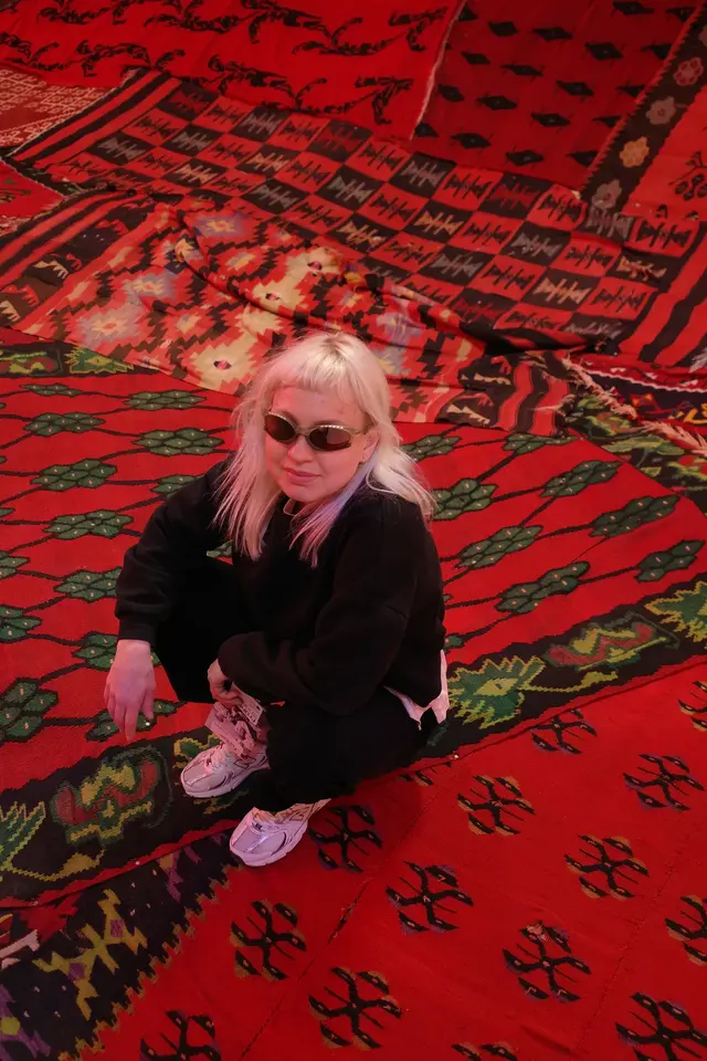 A person with light hair lying on a red patterned rug, looking up