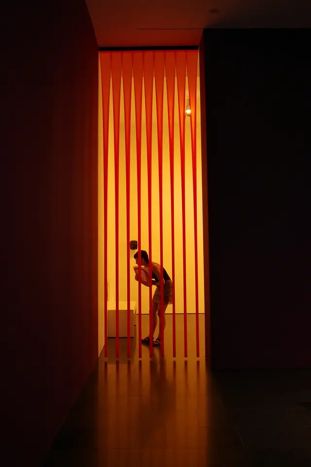 A silhouette of a person in a dark hallway lit by a tall orange opening