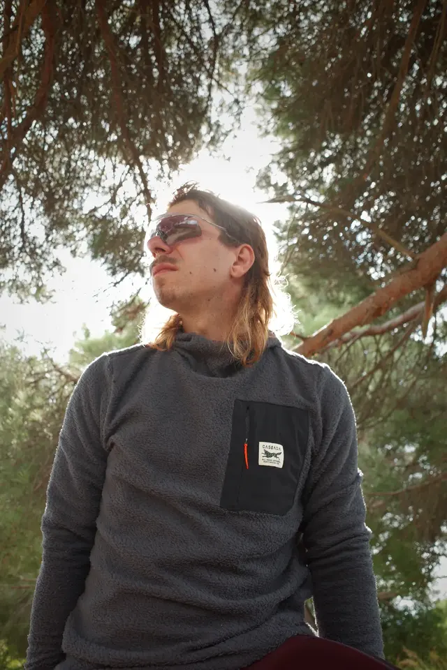 A close portrait of a person in a grey sweatshirt among pine trees